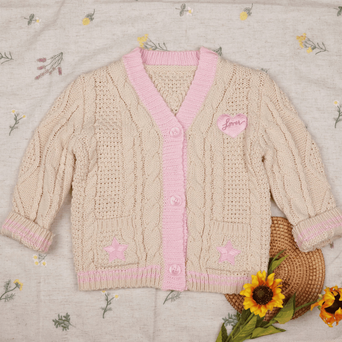 Knitted cardigan with pink trim and heart details on a floral-patterned fabric background.