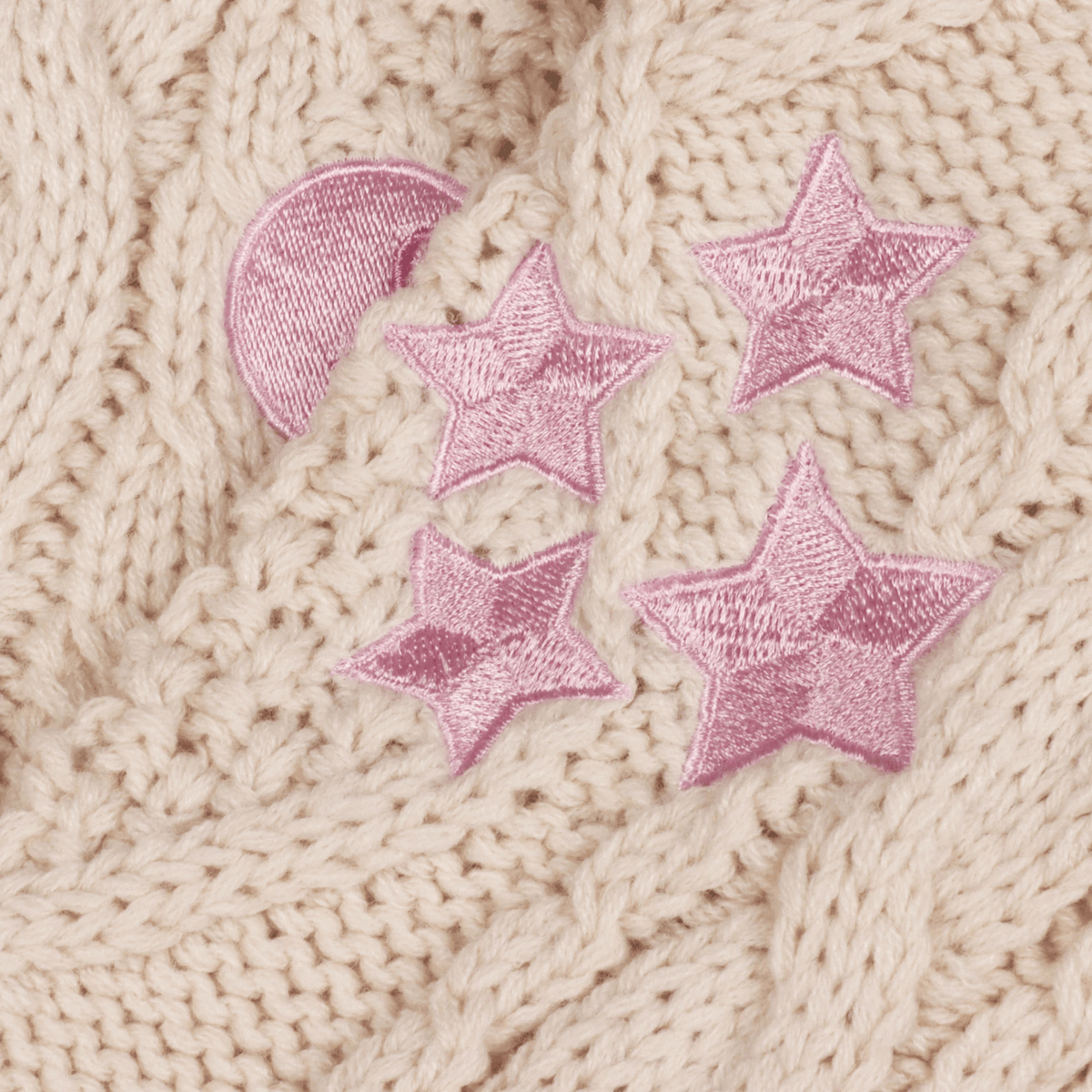 Close-up of a beige knitted fabric with pink embroidered stars and a pink crescent moon.