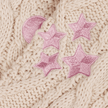 Close-up of a beige knitted fabric with pink embroidered stars and a pink crescent moon.
