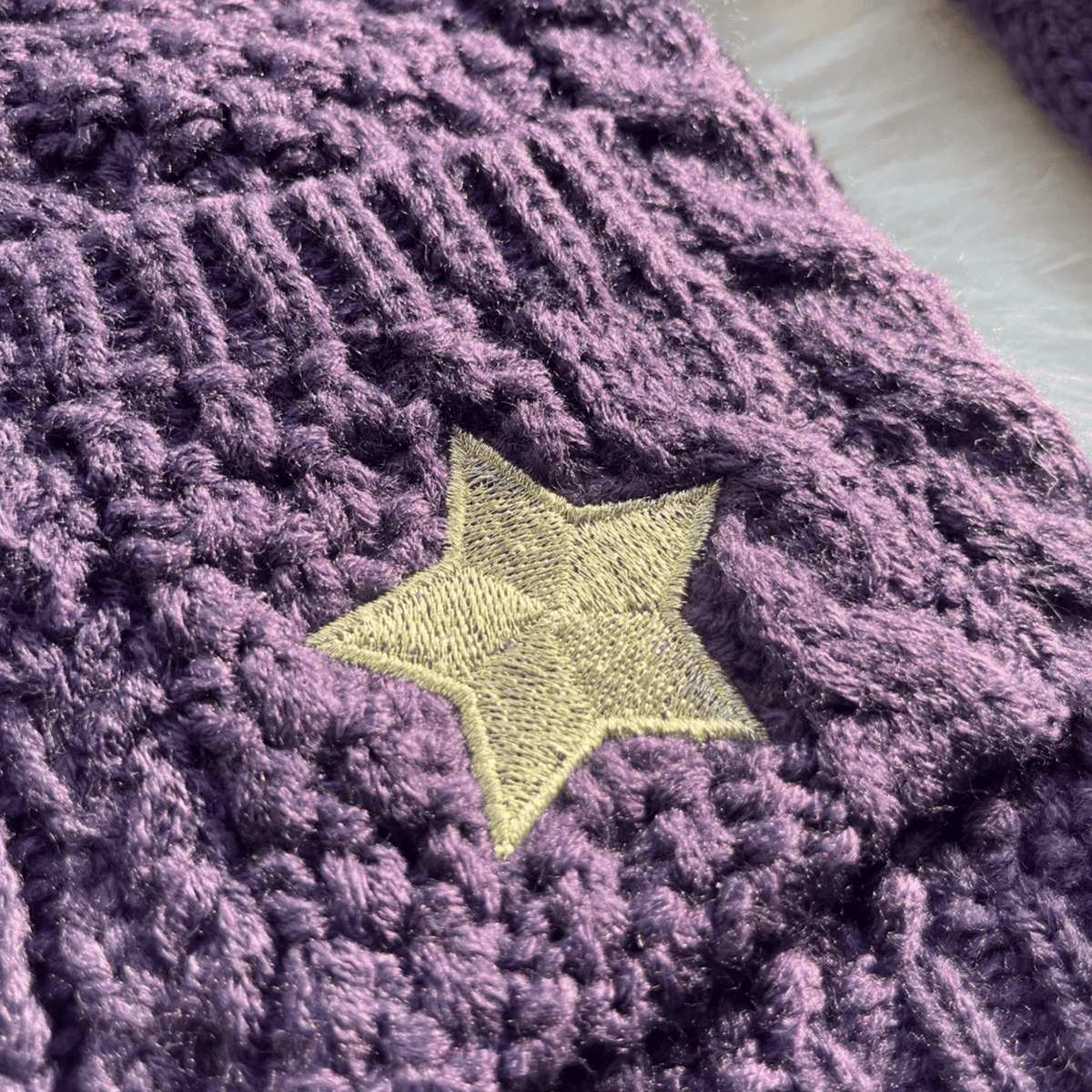Close-up of a purple textured fabric with a yellow star embroidered on it.