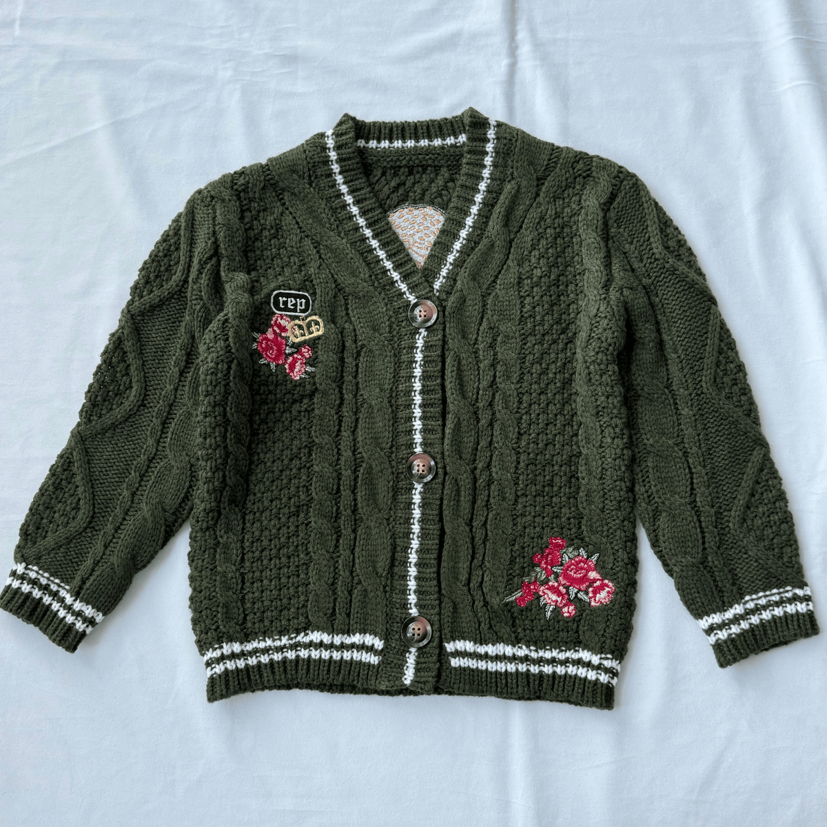 Green cardigan with floral embroidery and buttons on a light gray background