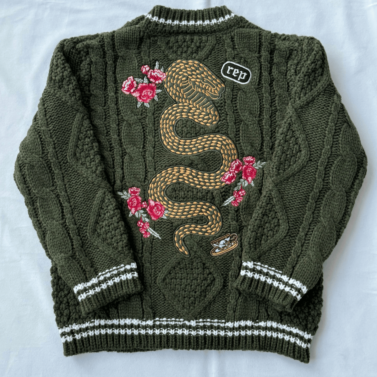 Green sweater with snake and floral embroidery on a white background