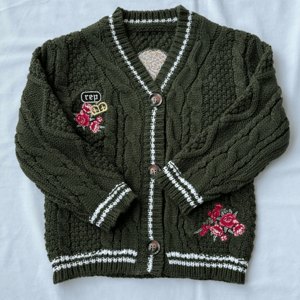 Green knitted cardigan with floral embroidery on a white background