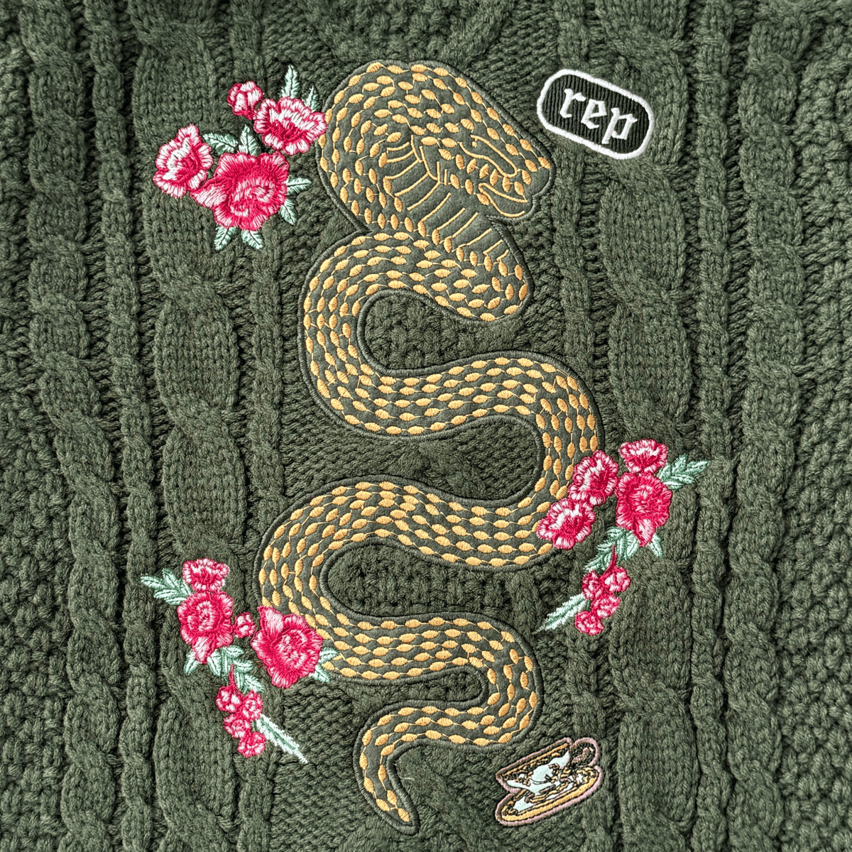 Embroidered snake design on a textured green fabric with pink flowers.