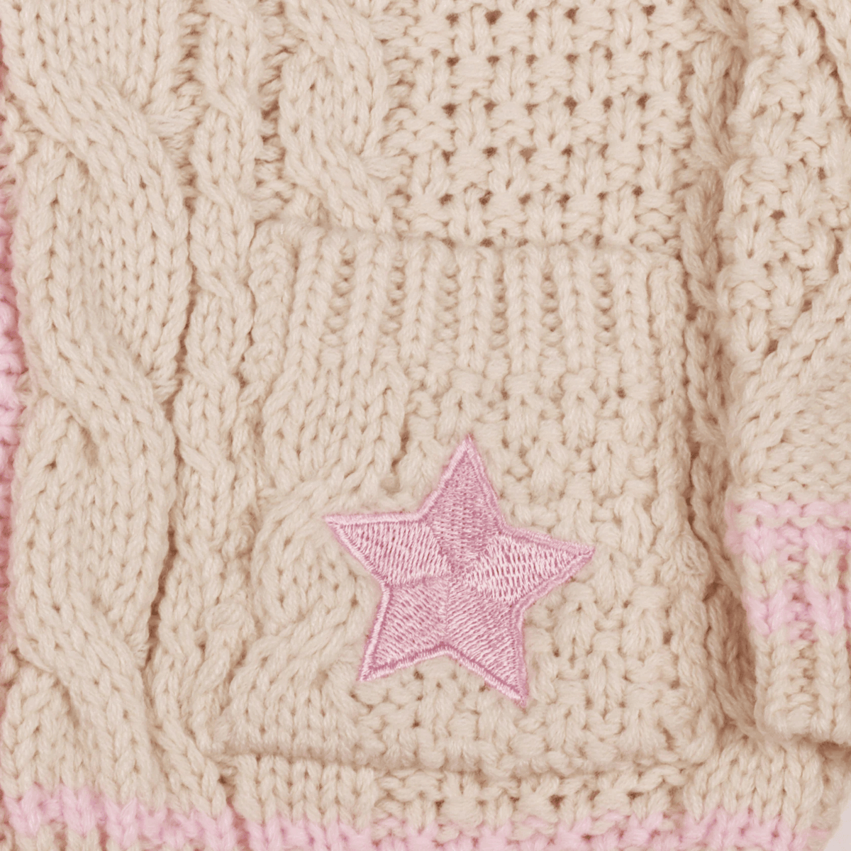 Close-up of a beige knitted fabric with a pink embroidered star.